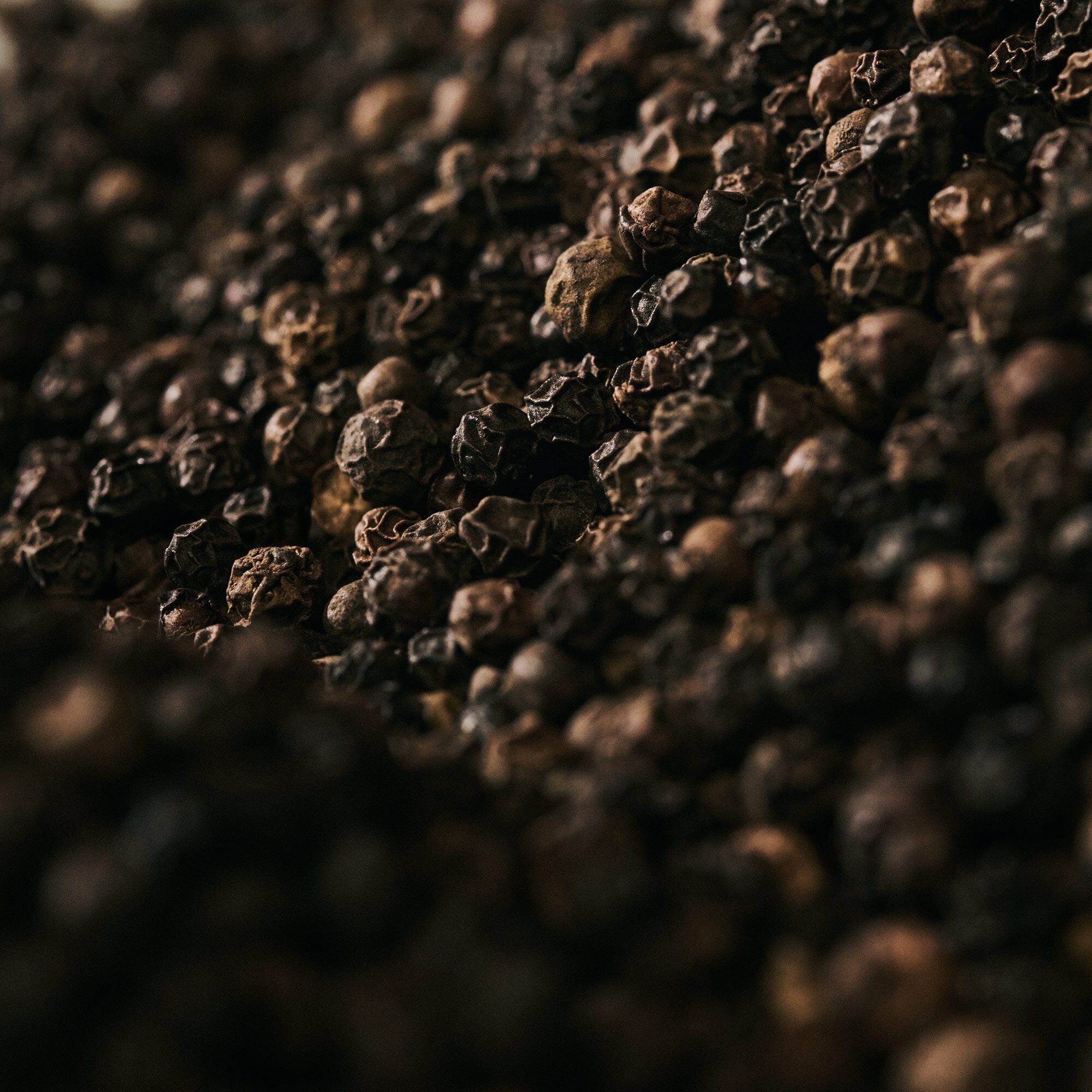 Close-up of black peppercorns scattered across a dark textured surface.