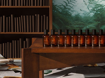 Amber glass bottles lined up on a wooden table in a room with a bookshelf and forest mural.