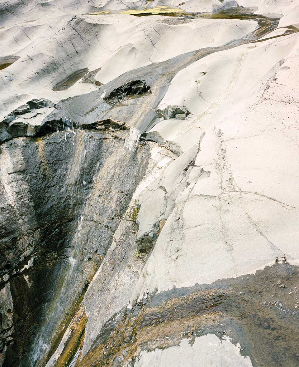 Pale weathered rock face with flowing mineral patterns and striations.