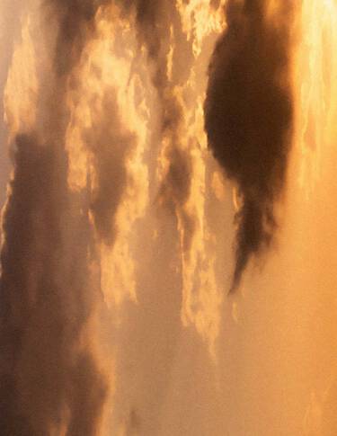 Golden sunset sky with layered clouds in warm amber tones, soft diffused light, and darker cloud forms crossing the scene.