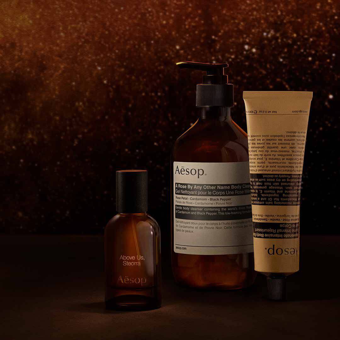 Aesop Above Us, Steorra bottle with pump bottle and tube against a warm speckled brown backdrop.