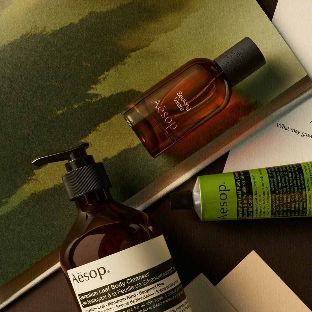 Aesop Seeking Virere bottle with pump bottle and green tube arranged on papers with painted green imagery.