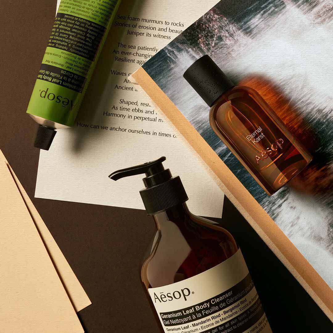 Aesop Eternal Karst bottle with pump bottle and green tube arranged on papers with foaming water imagery.