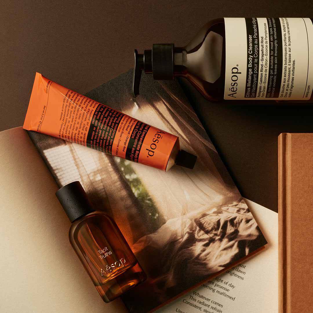 Aesop Tacit Truths bottle with pump bottle and orange tube arranged on papers with a monochrome image.