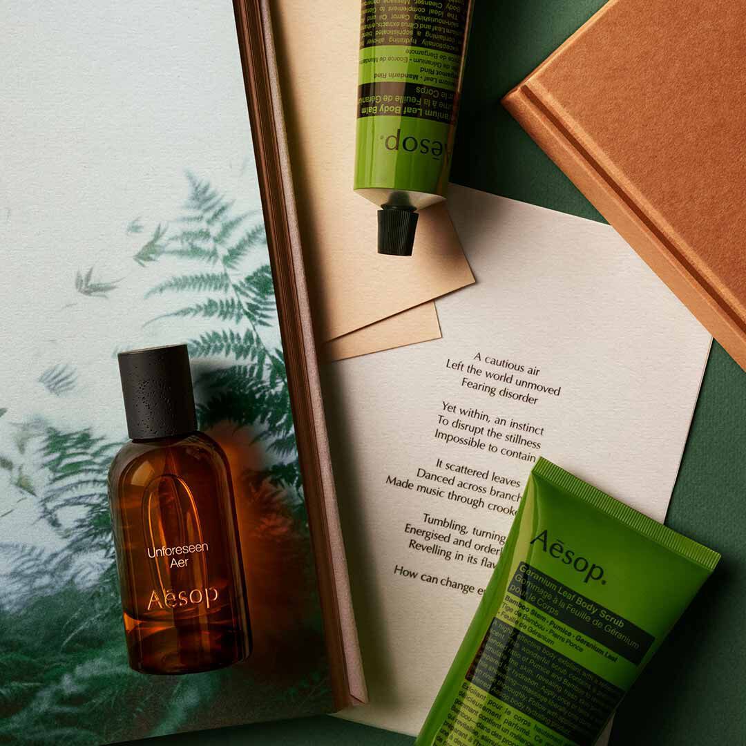 Aesop Unforeseen Aer bottle with pump bottle and green tube arranged on papers with fern imagery.