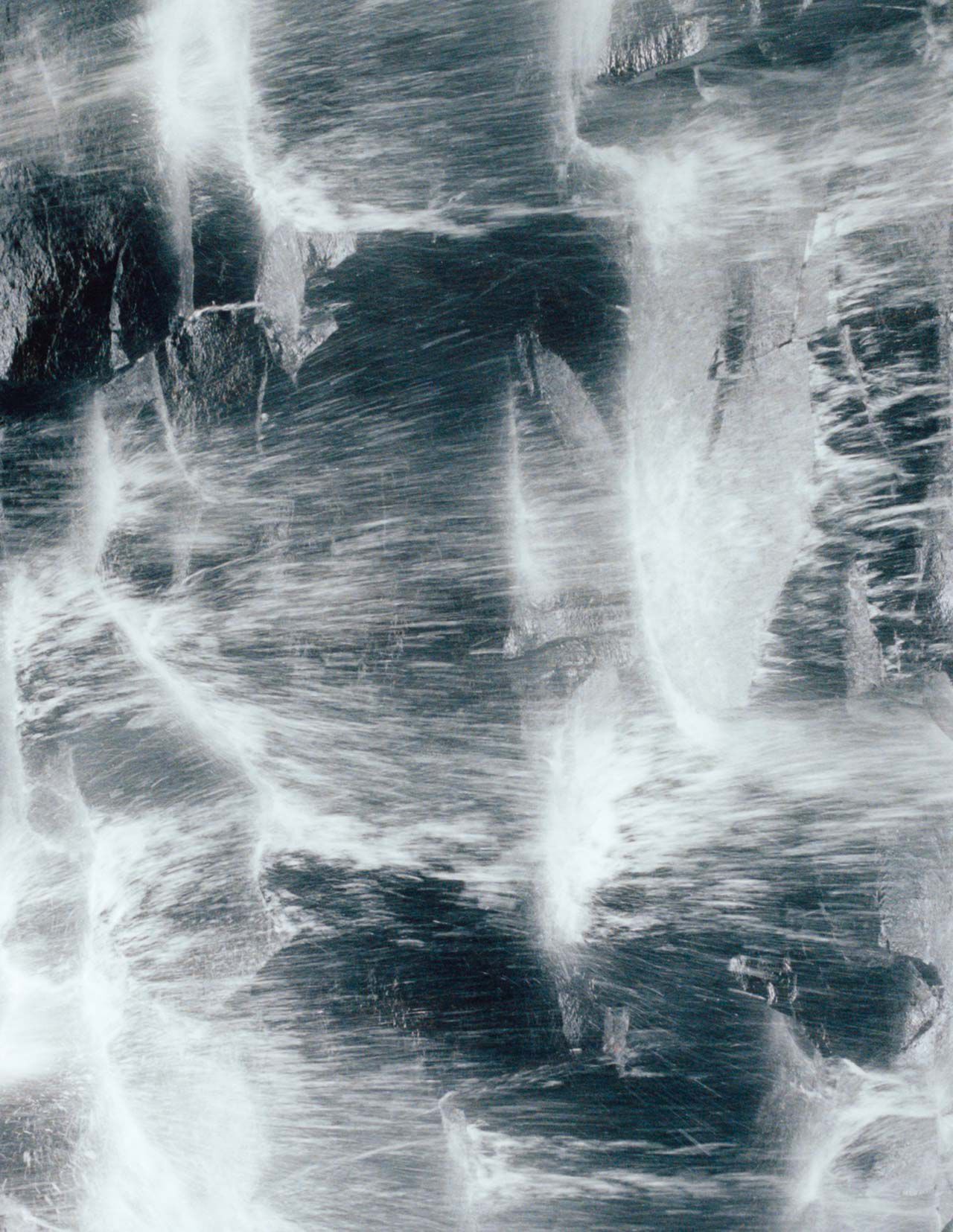 Dark blue-grey rock surface with white vein-like streaks and rough mineral texture, forming a high-contrast marbled pattern.