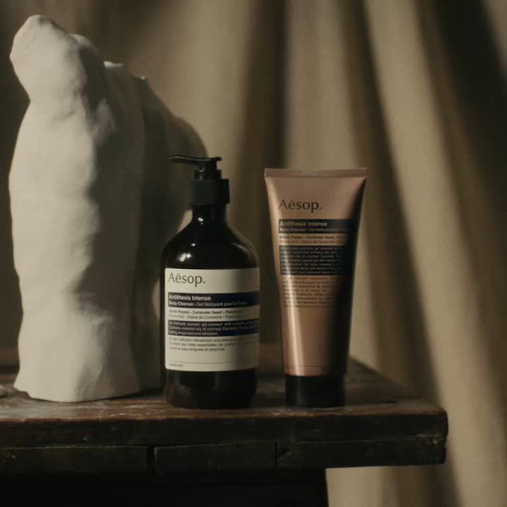 Aesop Antithesis Intense Body Cleanser pump bottle and tube beside a white torso sculpture on a wooden work table.