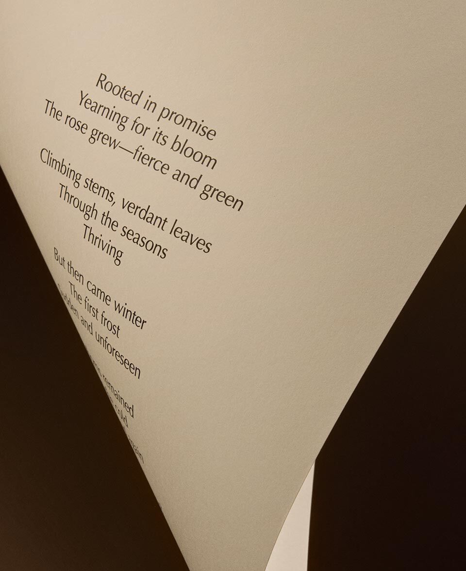 Triangular fold of cream paper showing poem text against a dark backdrop.