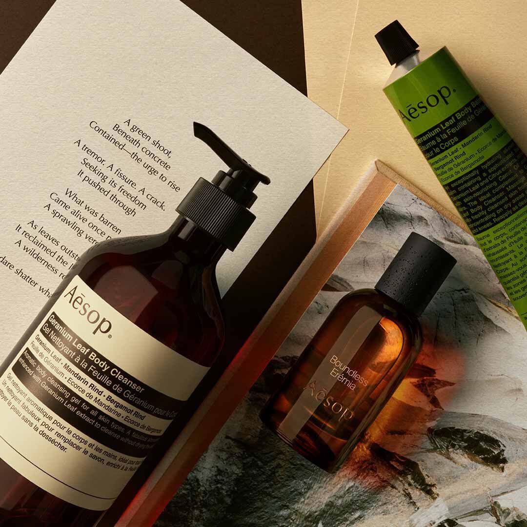 Aesop Boundless Eremia bottle with pump bottle and green tube arranged on papers and a stone image.